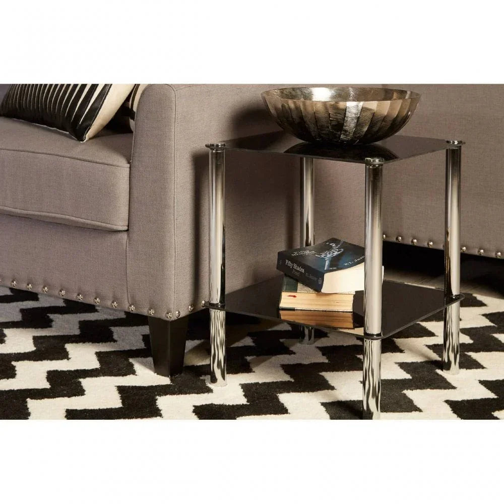 Chrome and glass side table with books and a decorative bowl beside grey sofa on patterned rug