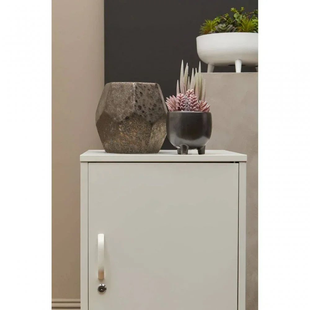 White cabinet with chrome handle topped with a stone vase and a black plant pot with succulents