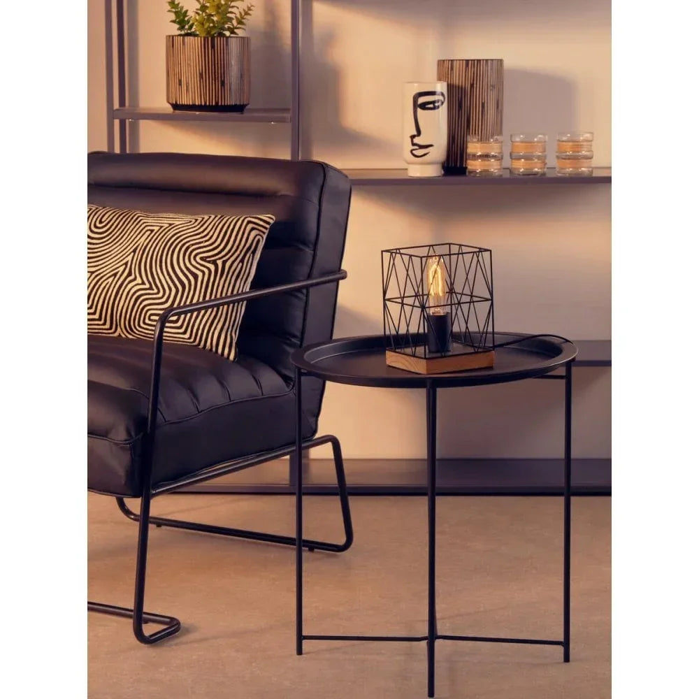 Black metal accent chair with patterned cushion beside round black side table and wire lamp