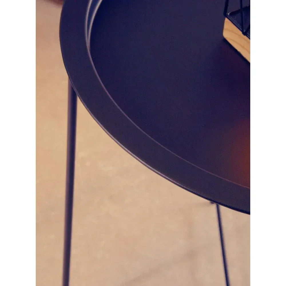 Black metal side table with round top and slim legs, close-up of edge and surface