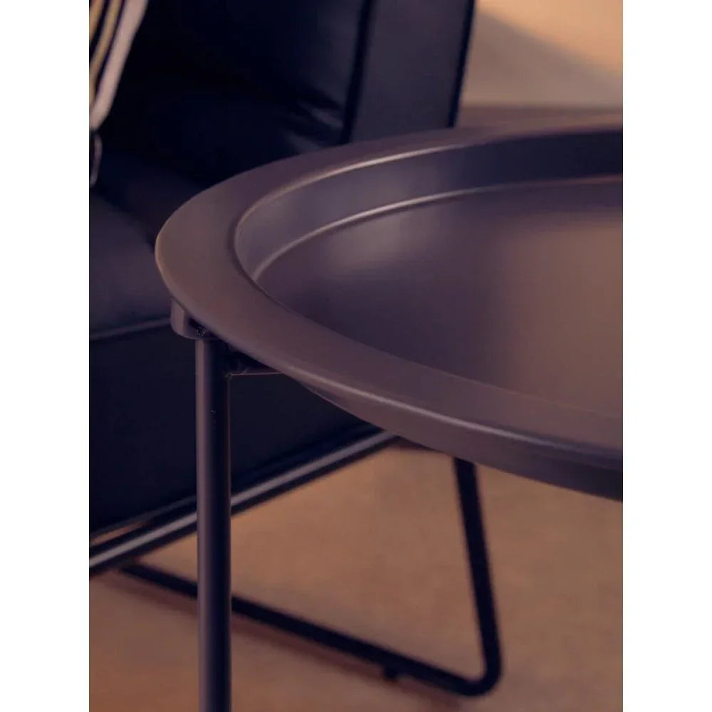 Round black metal side table with raised edge beside modern black armchair