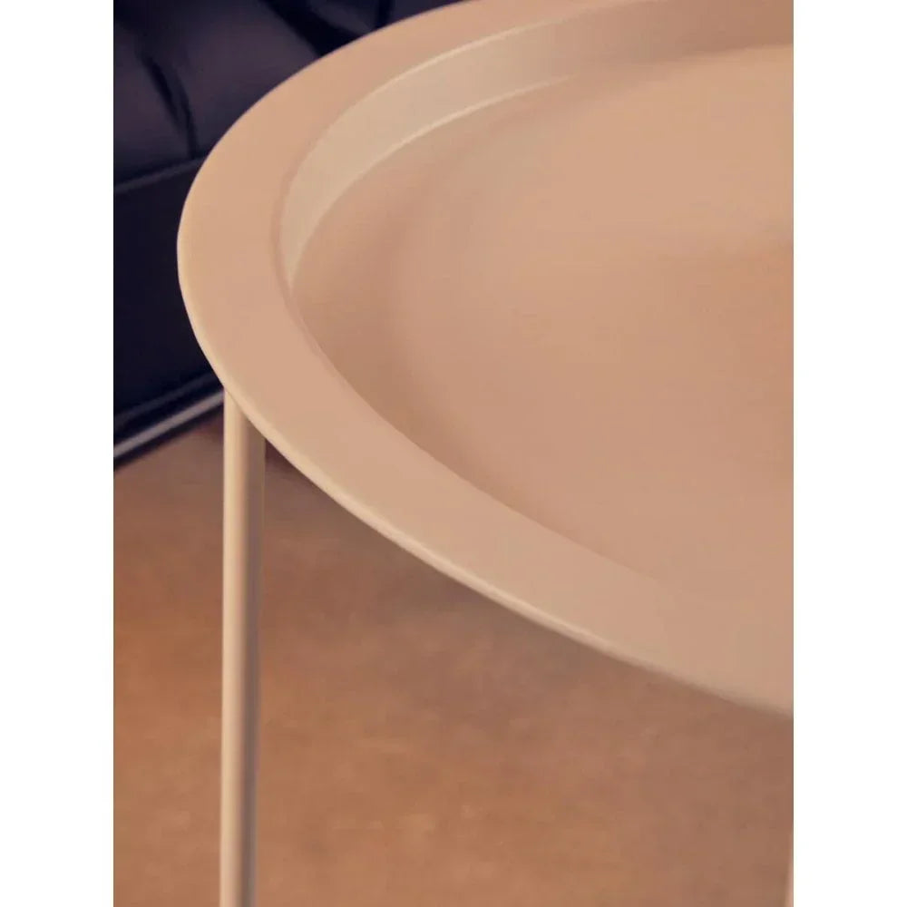 Round beige metal side table with raised edge and slim legs, close-up angle