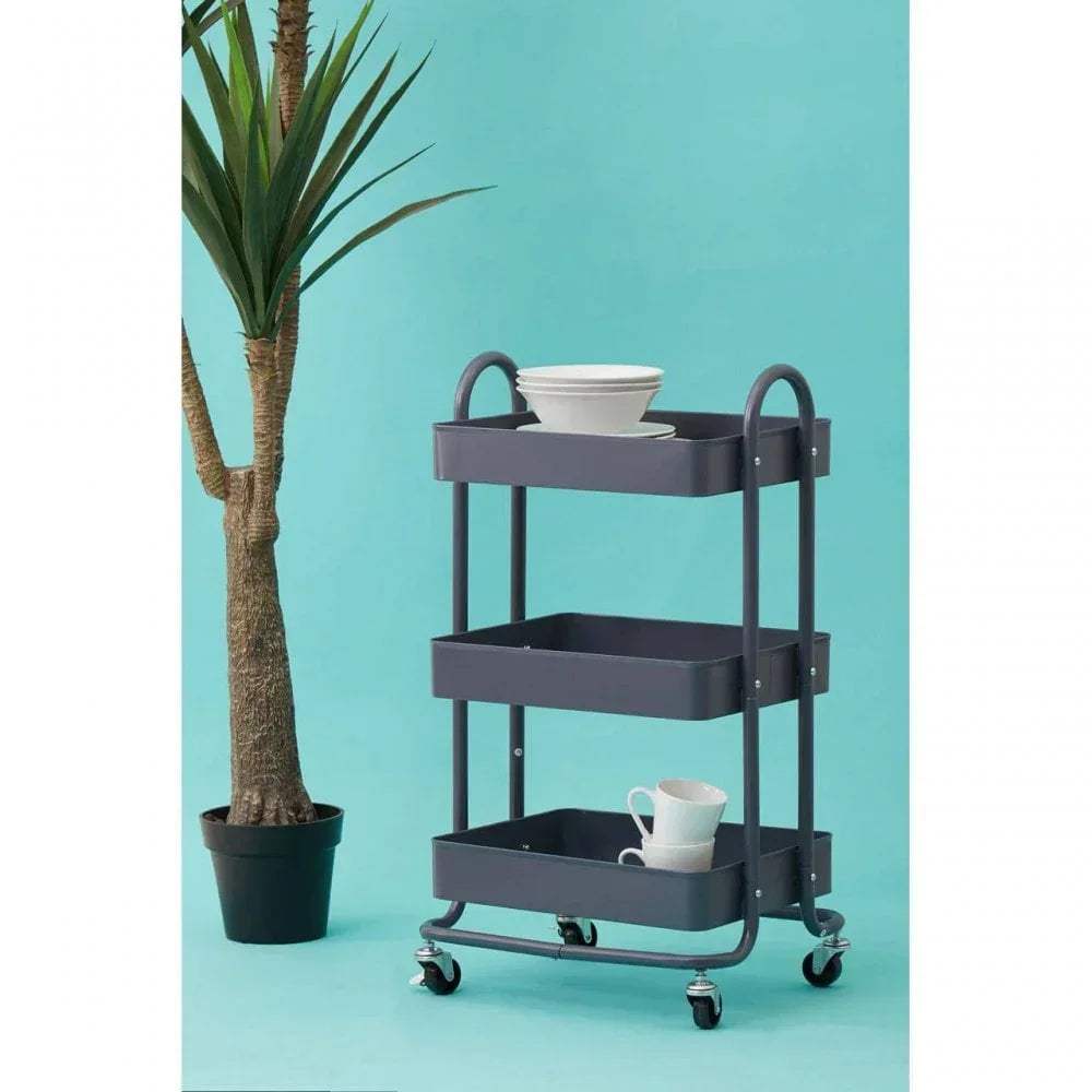 Three tier kitchen trolley with dishes on wheels beside indoor plant, blue background