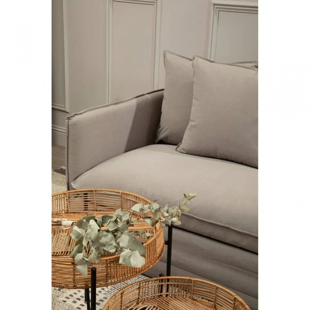 Light grey sofa with soft cushions beside round wicker coffee tables and green foliage
