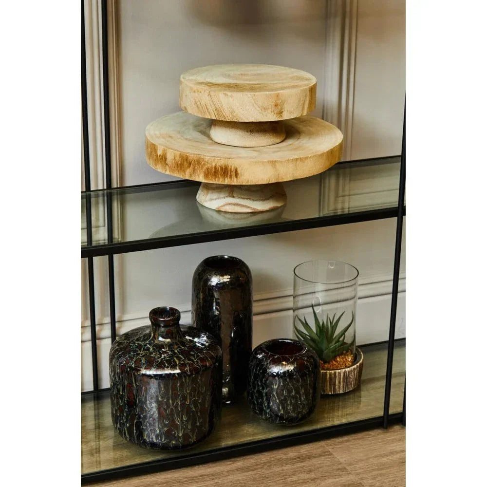 Wooden decorative cake stands on glass shelf beside black vases and glass terrarium