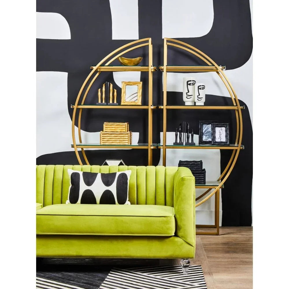 Green velvet sofa in front of gold round shelving unit with modern decor accessories