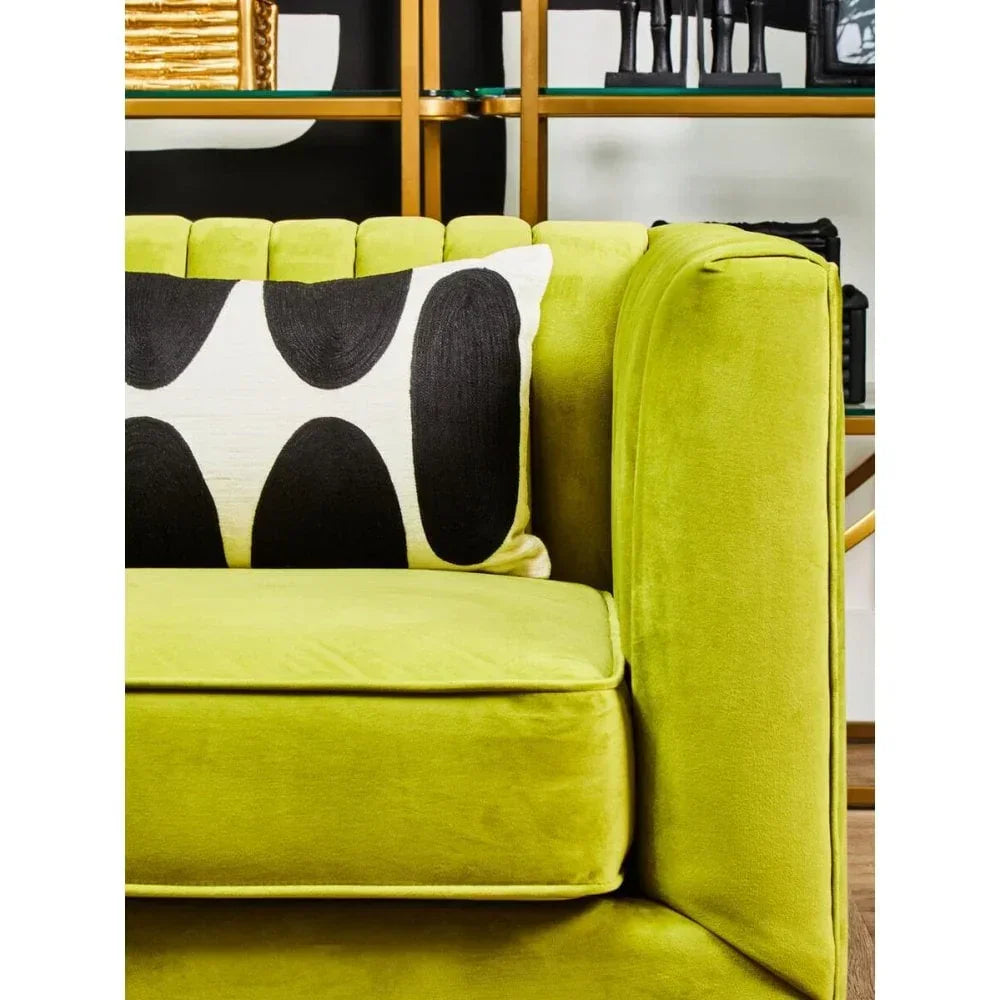 Lime green velvet sofa with black and white geometric cushion near gold shelving