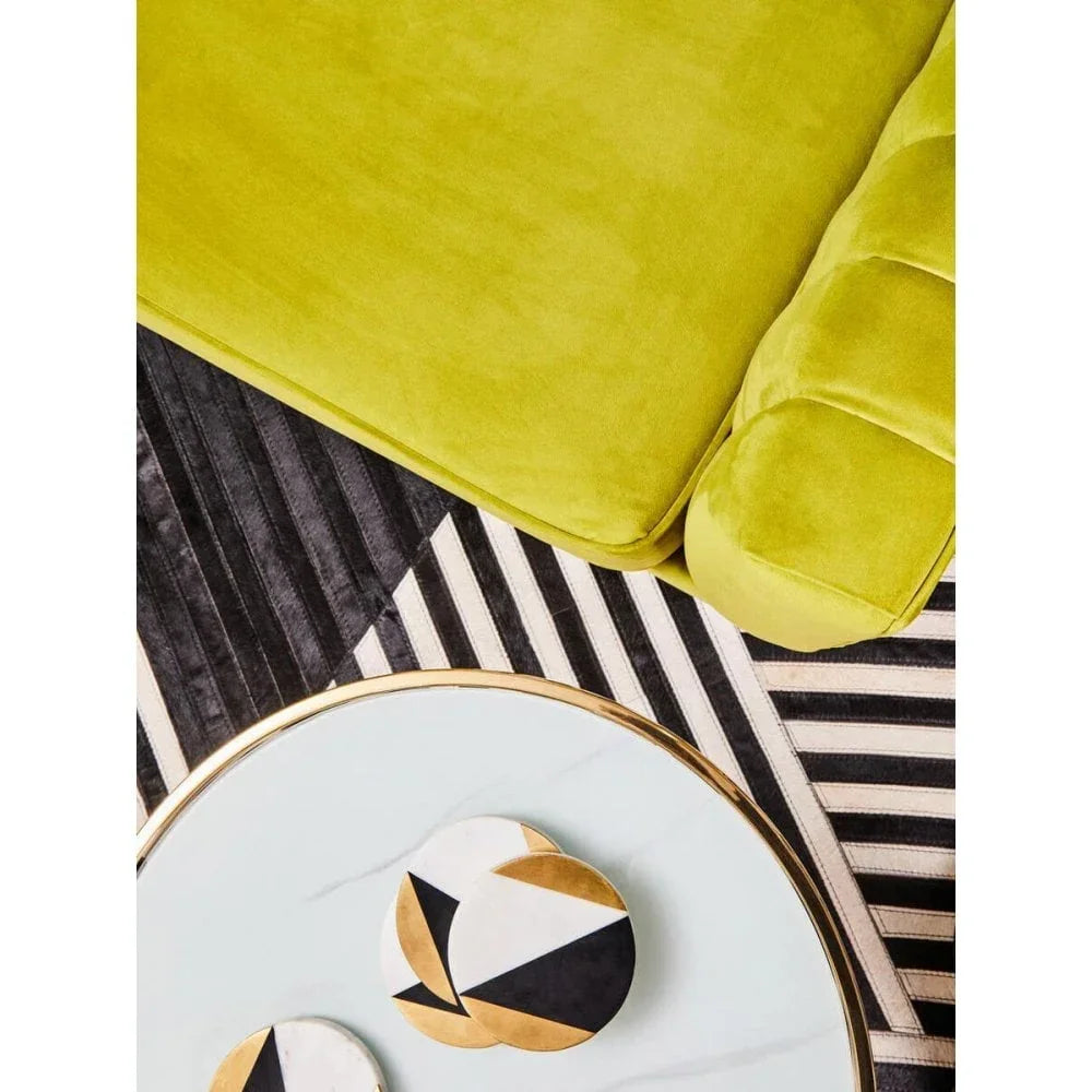 Lime green velvet sofa with tufted armrest beside round coffee table on striped rug