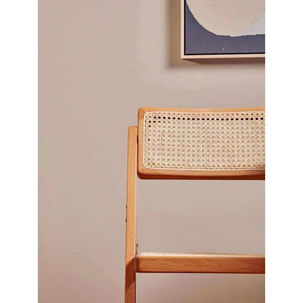 Wooden dining chair with woven cane backrest against neutral wall and abstract artwork