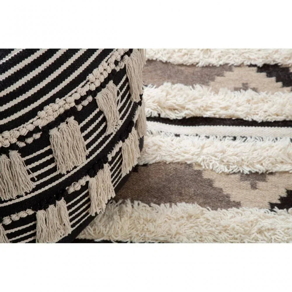 Striped black and cream pouffe with tassels beside textured geometric rug
