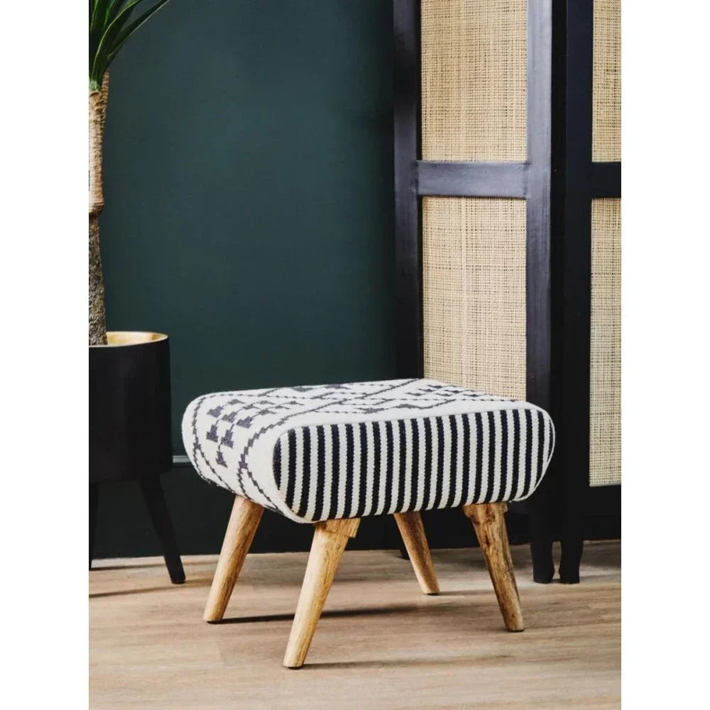 Patterned fabric footstool with wooden legs on wooden floor beside black screen