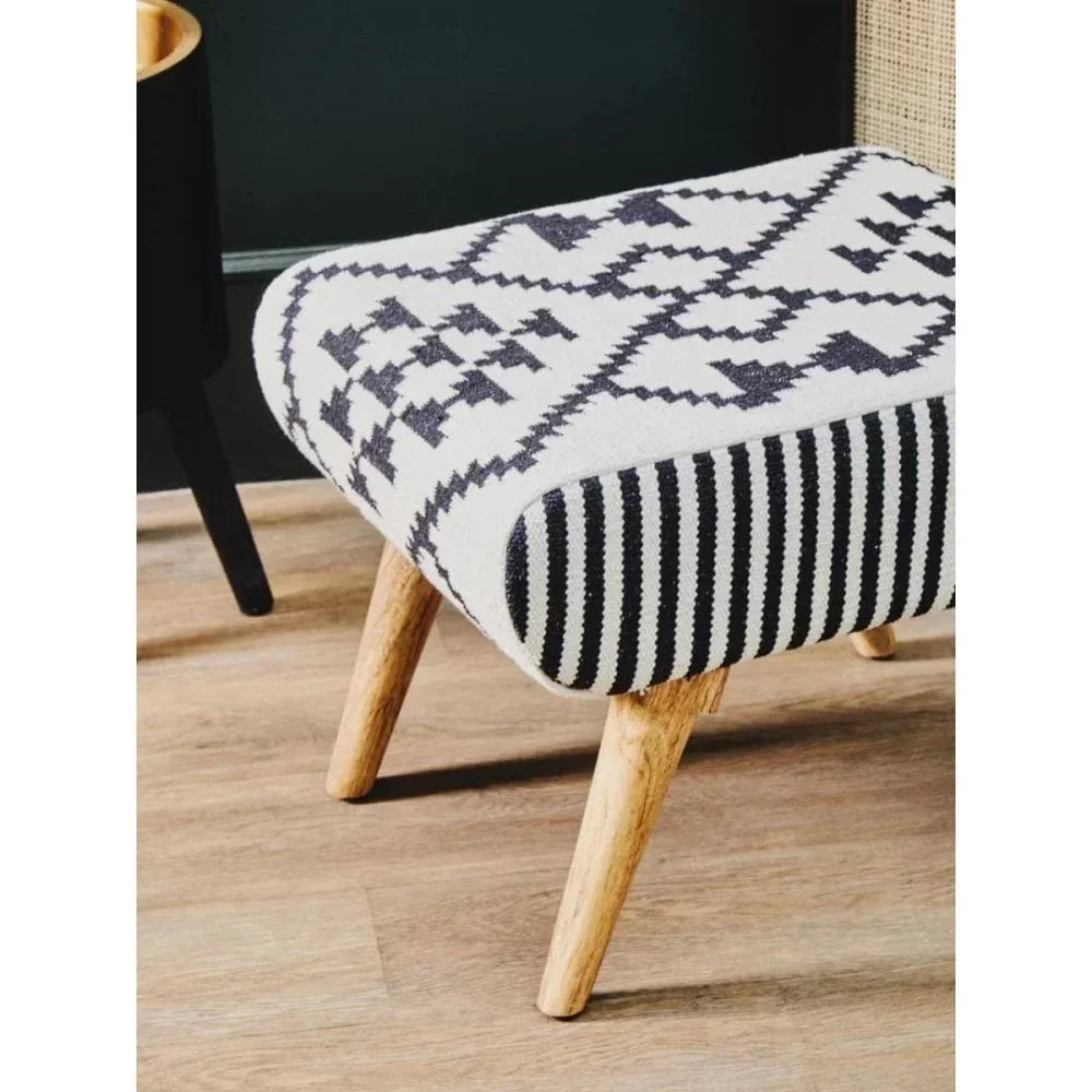 Patterned footstool with black and white geometric fabric and wooden legs on laminate floor