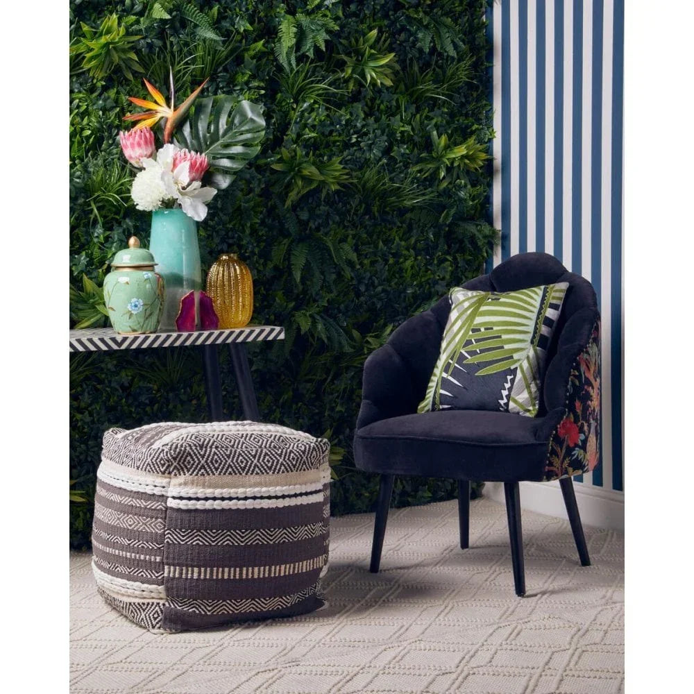Black velvet accent chair with patterned cushion beside geometric pouffe and striped table