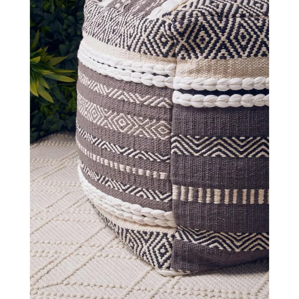 Textured fabric pouffe with geometric black and cream pattern on woven rug