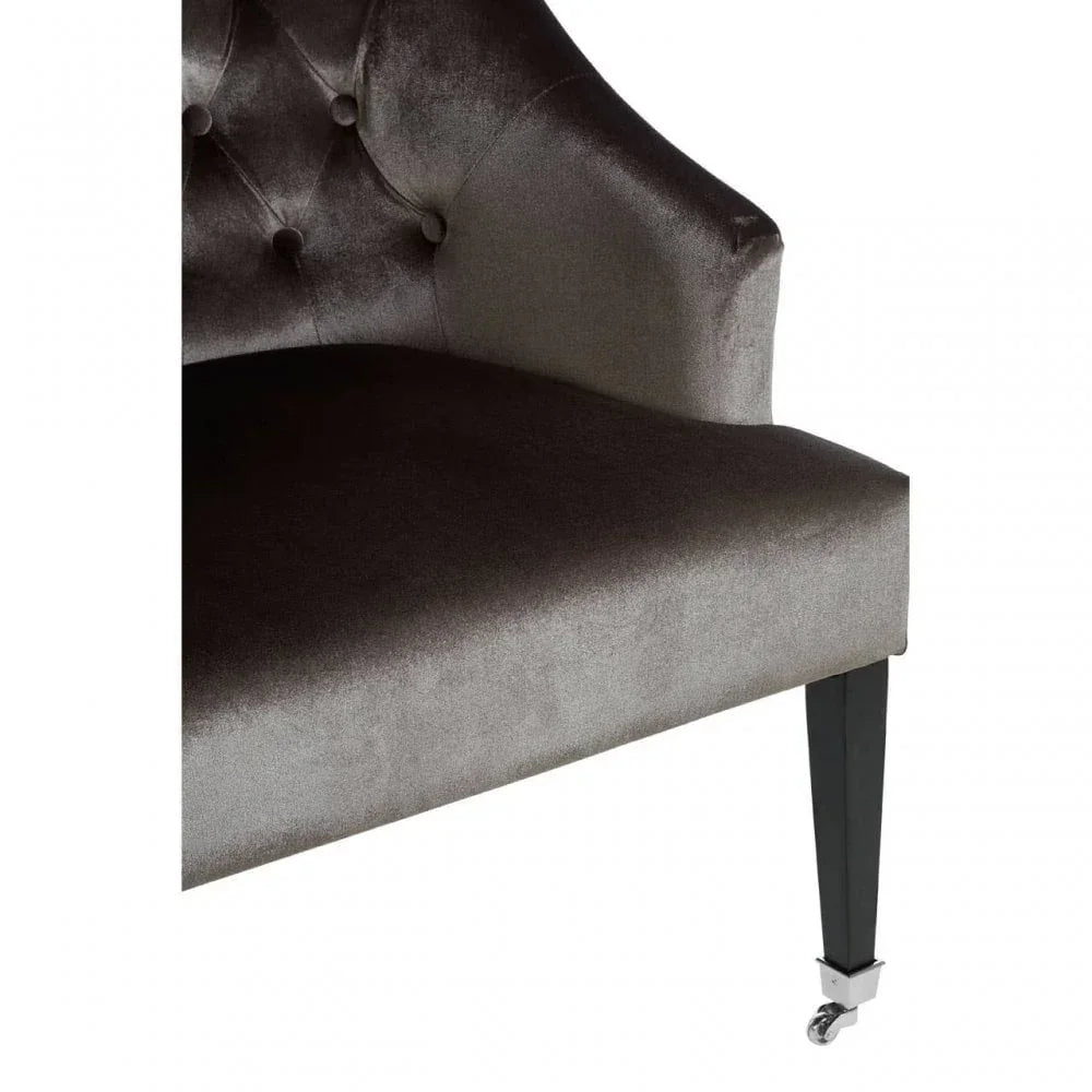 Close-up of tufted velvet chair seat with slender black leg and metal caster wheel