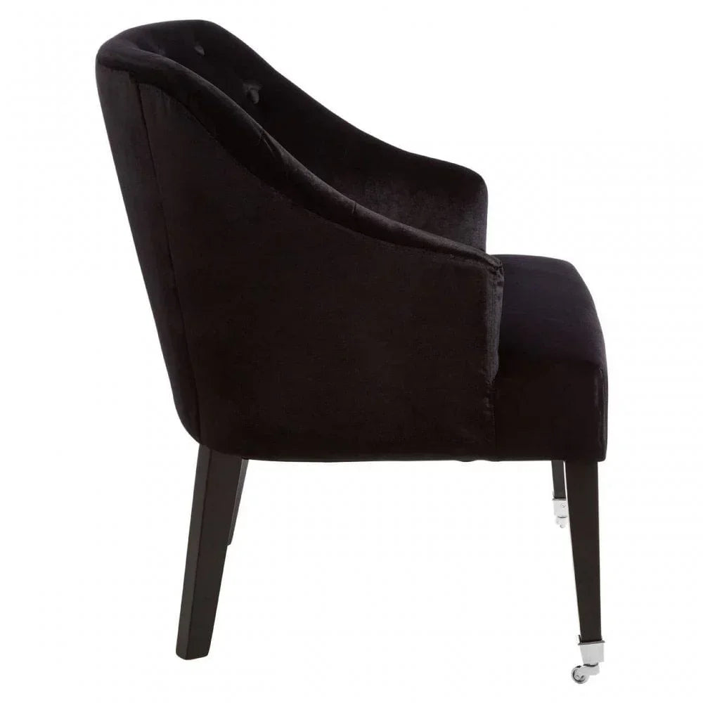 Black velvet dining chair side view with curved back and dark wood legs, front wheels visible