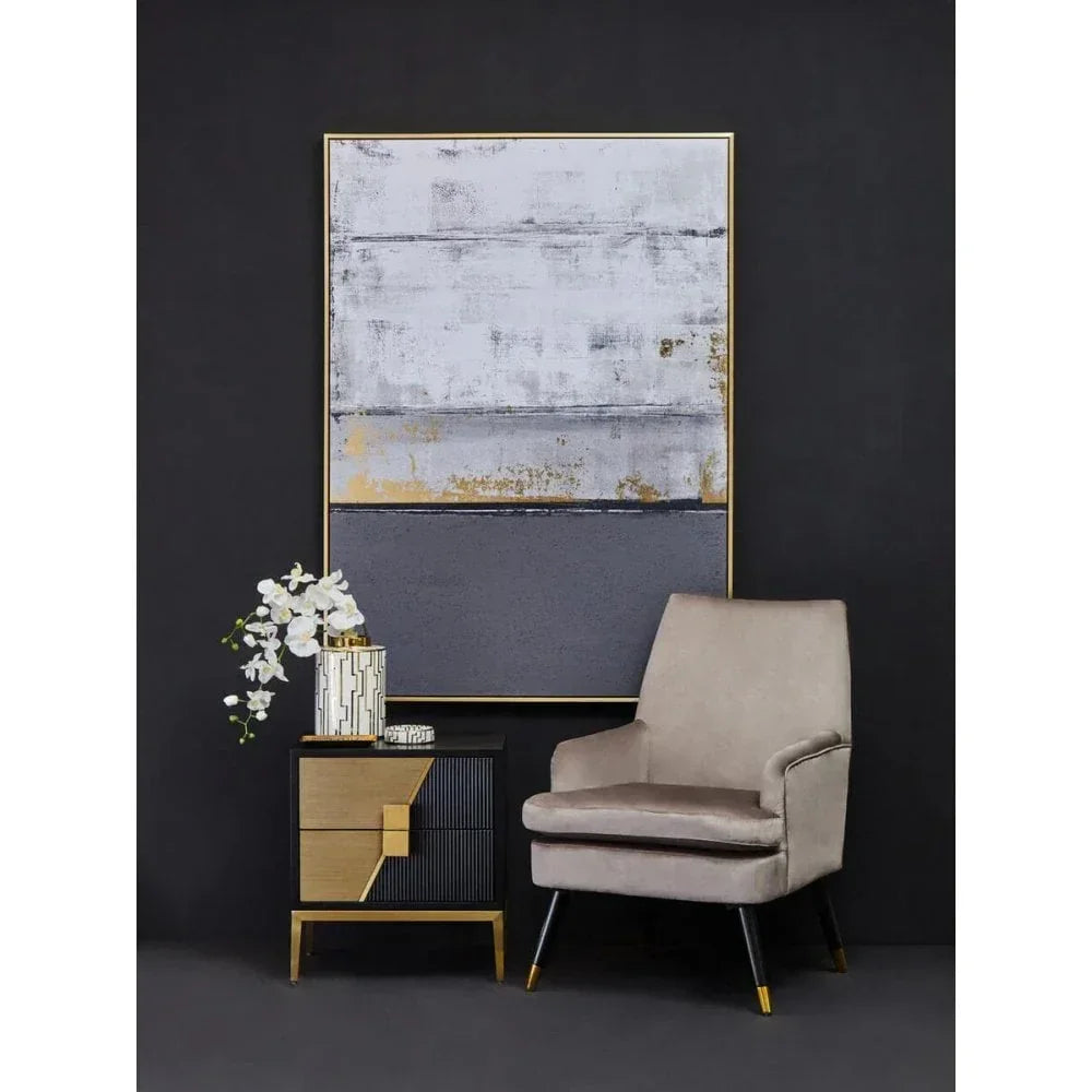 Modern beige armchair next to black and gold side table with vase and abstract wall art