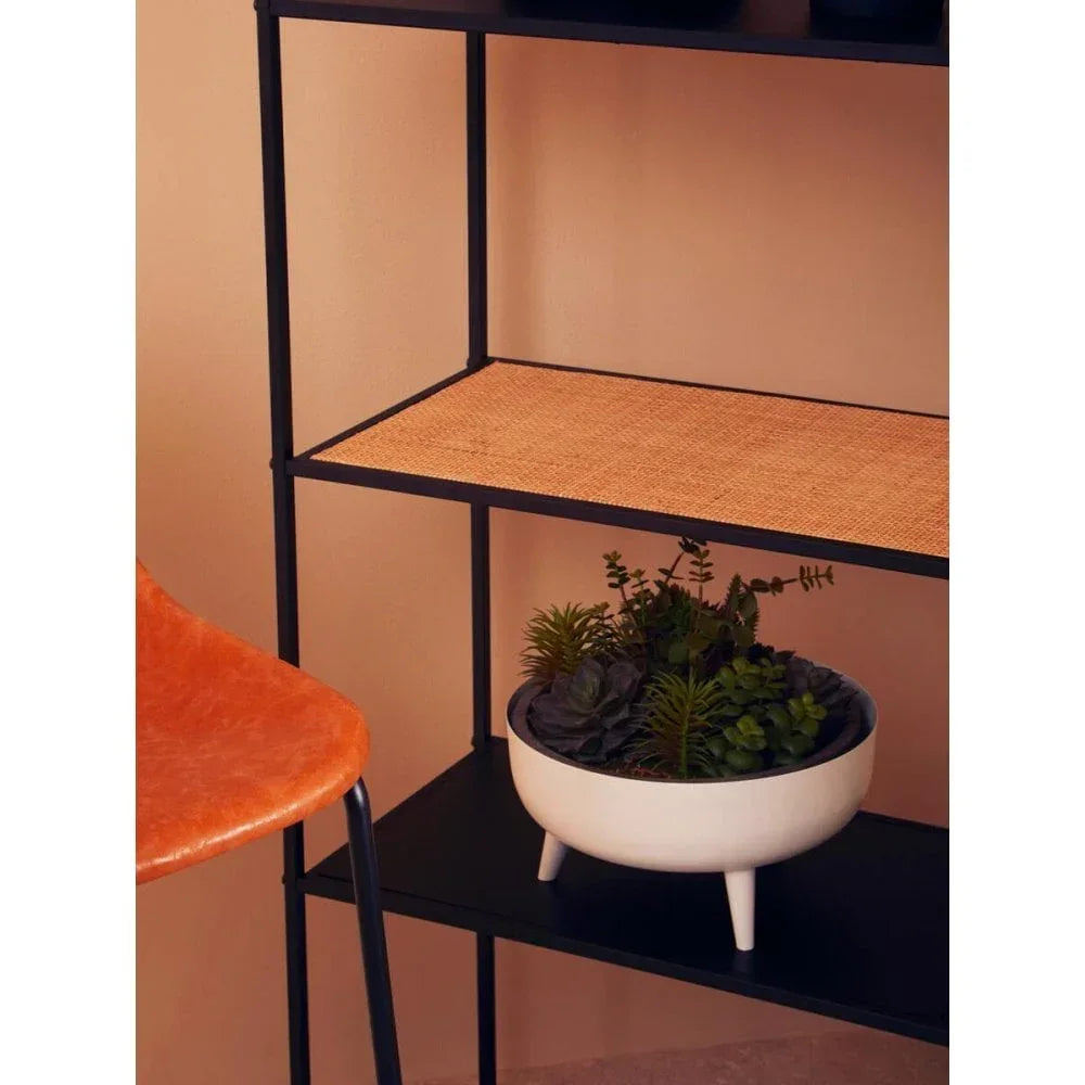Black metal shelving unit with rattan shelf and planter, next to orange dining chair