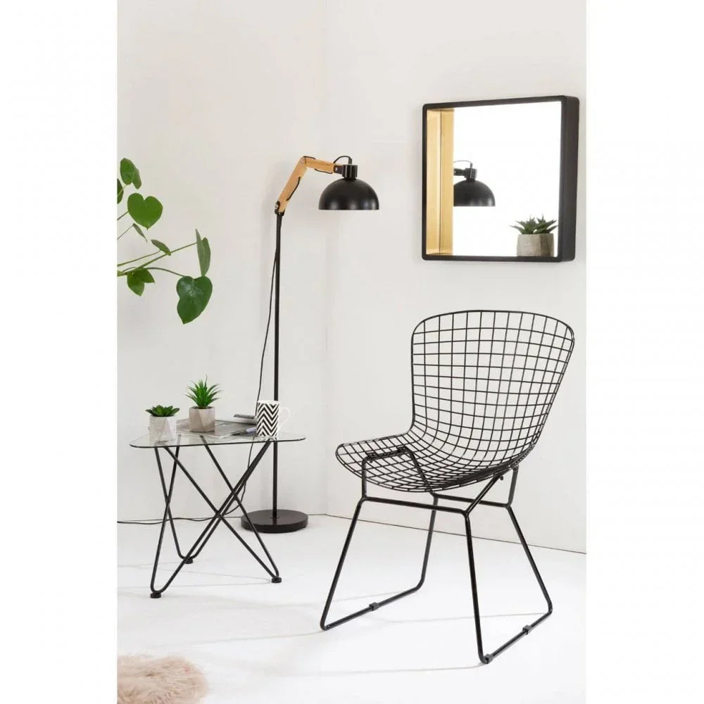 Black wire accent chair with glass side table, floor lamp, and wall mirror in modern setting