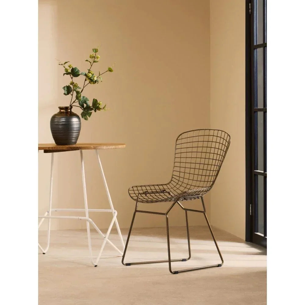 Black wire dining chair beside wooden table with vase in modern room