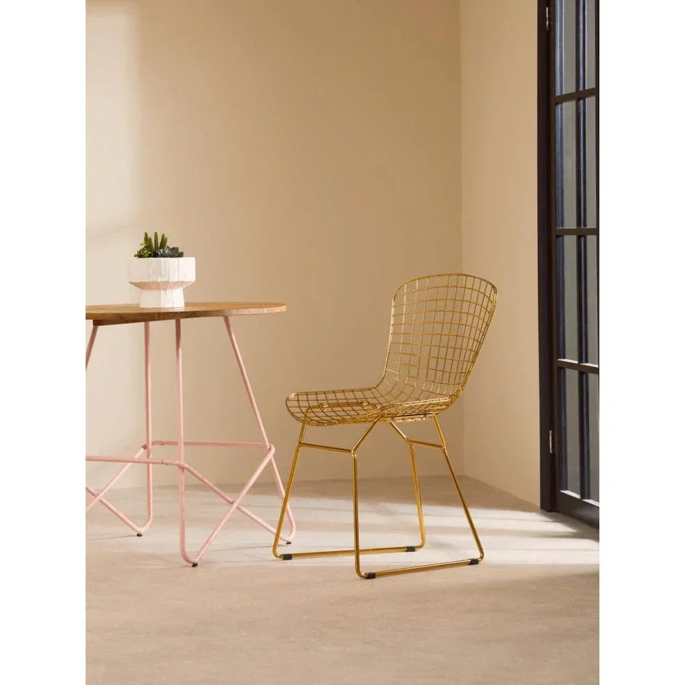Gold metal dining chair with grid design beside light wood table and potted plant