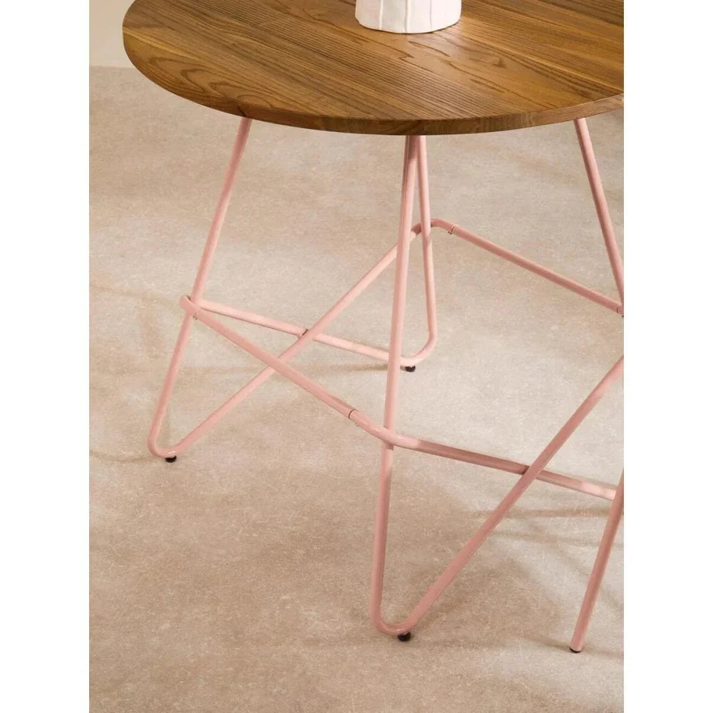 Round wooden dining table with pink metal legs on beige carpet