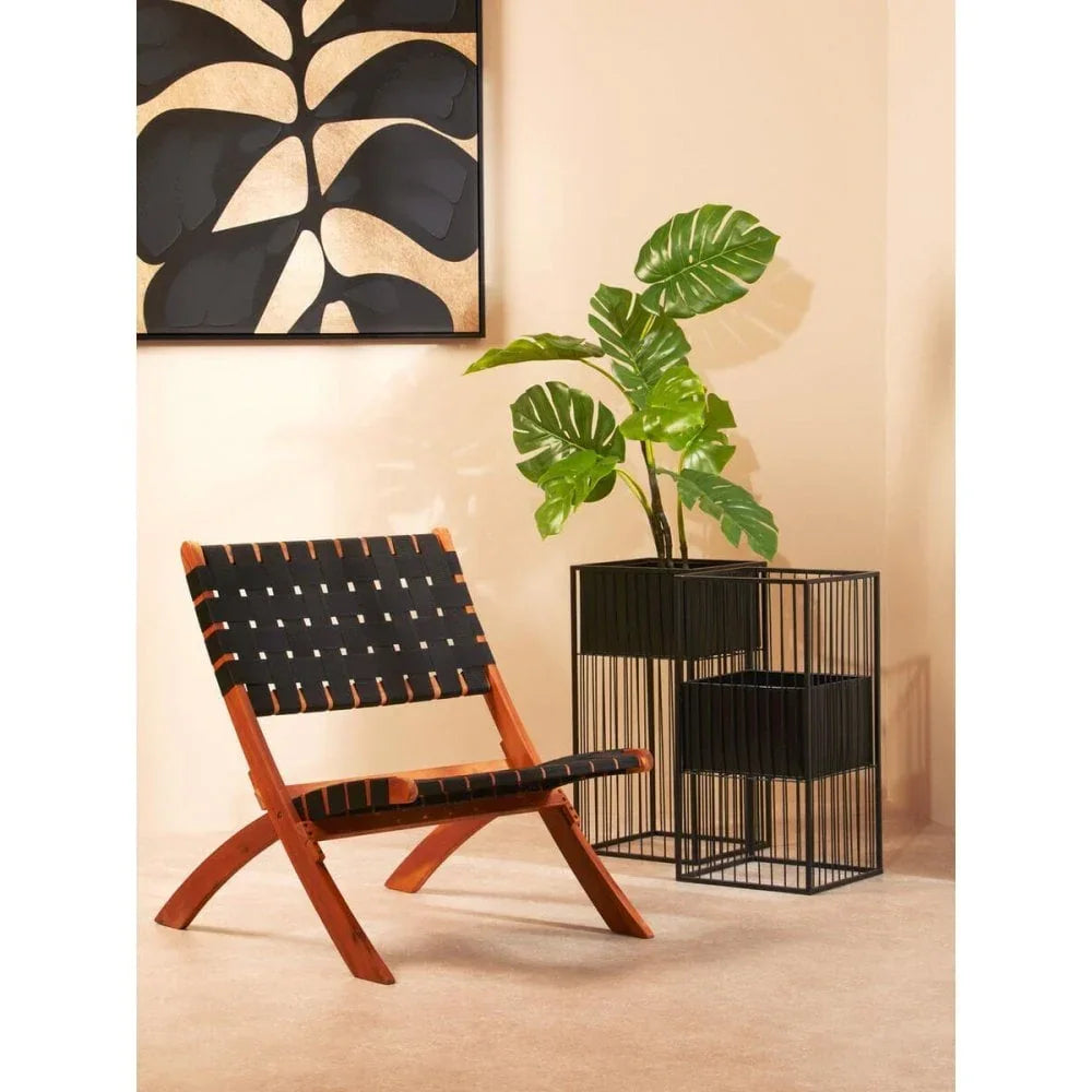 Wooden accent chair with black woven seat beside modern plant stand and abstract wall art