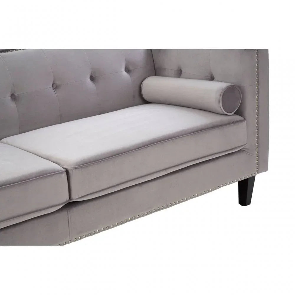 Light grey velvet sofa with button-tufted back, studded trim, and bolster cushion