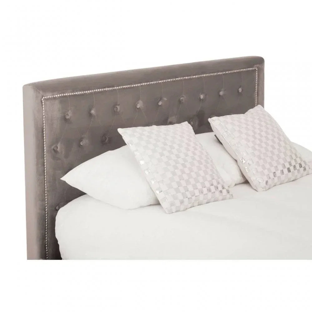 Grey velvet upholstered bed with button-tufted headboard and two white decorative cushions
