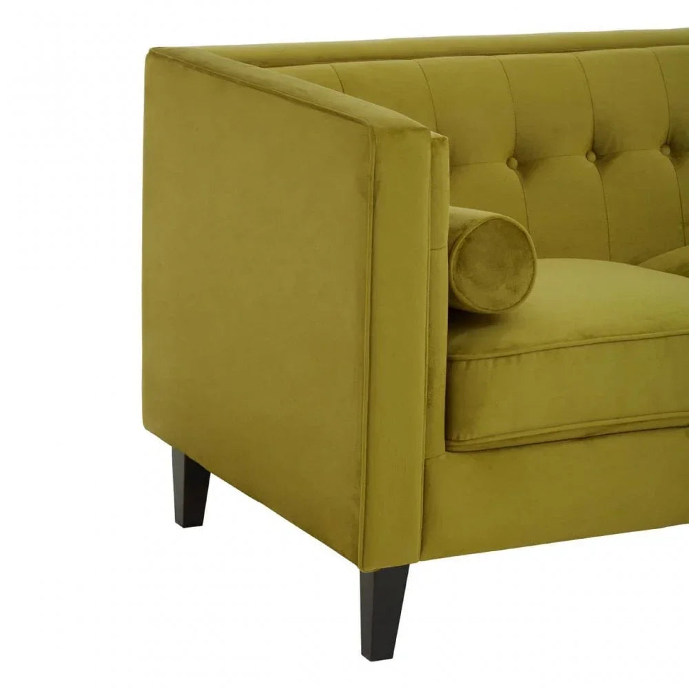 Green velvet sofa with buttoned backrest and cylindrical cushion, angled armrest view