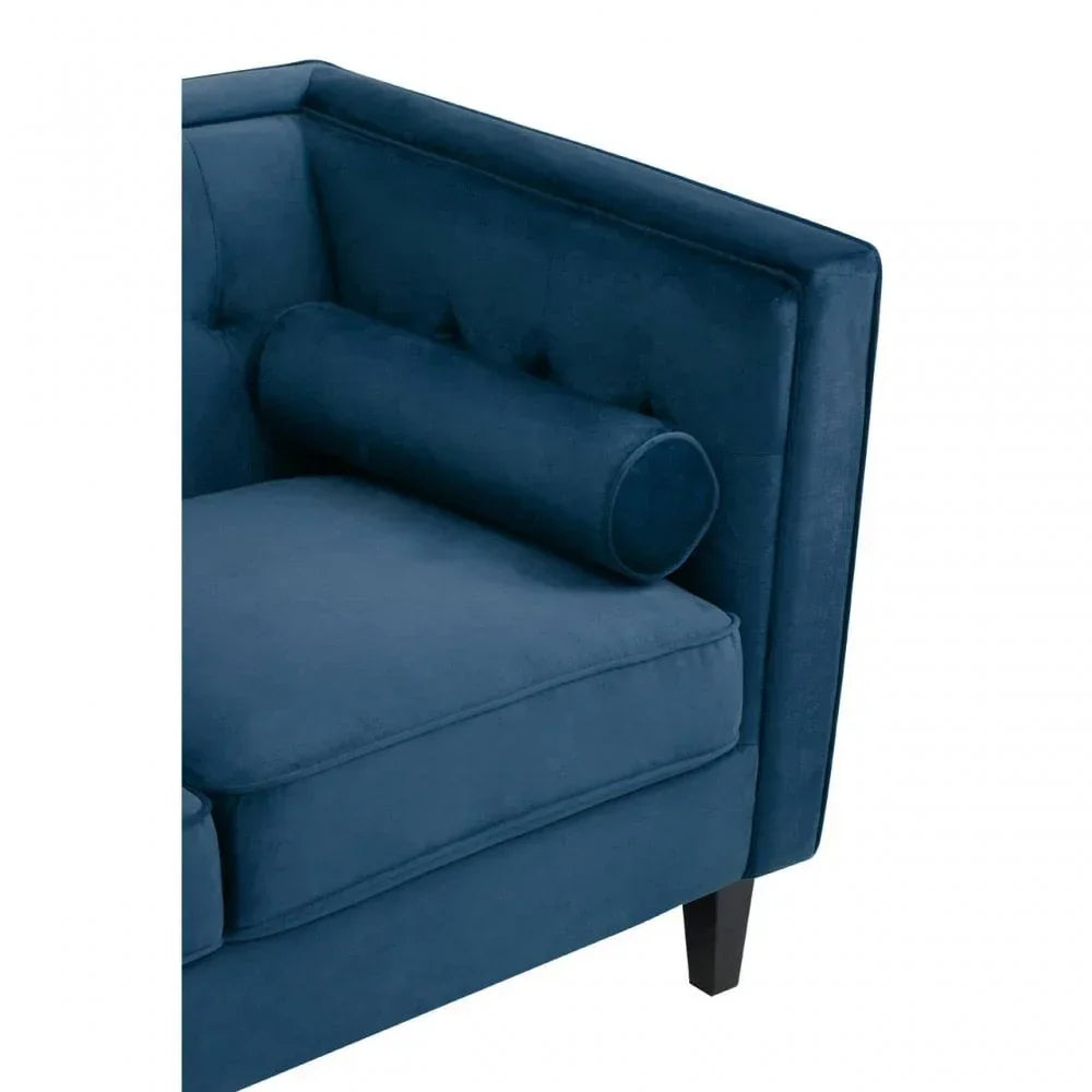 Corner view of blue velvet sofa with bolster cushion and dark wooden leg