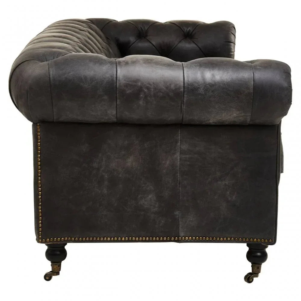 Side view of dark leather chesterfield sofa with button tufting and brass stud detailing