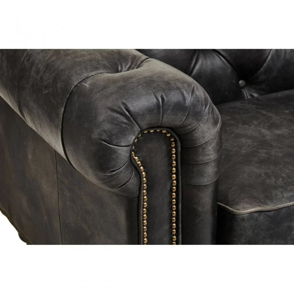 Closeup of black leather sofa arm with button tufting and brass stud detailing