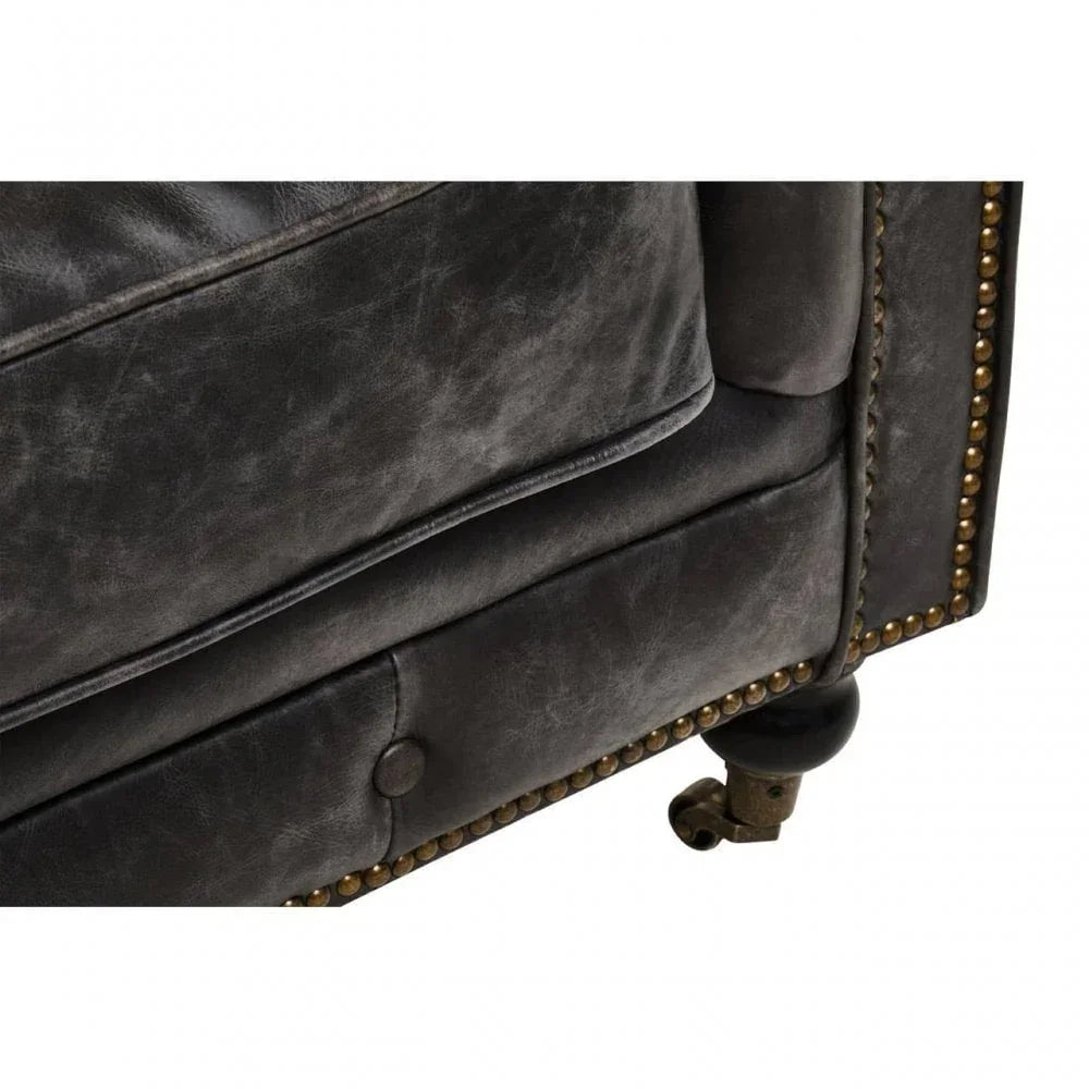 Close-up of black leather sofa corner with studded detail and wooden castor leg
