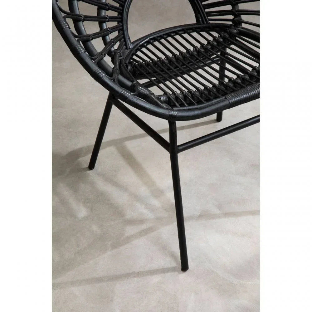 Black rattan dining chair with metal legs on light floor, close-up of seat and frame
