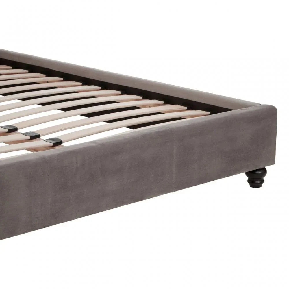Grey upholstered bed frame corner with wooden slats and dark turned legs