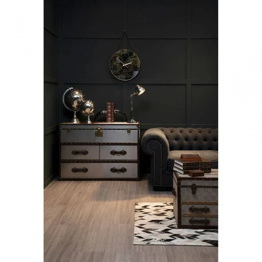 Grey trunk chest of drawers beside tufted sofa, with stacked books and vintage globes