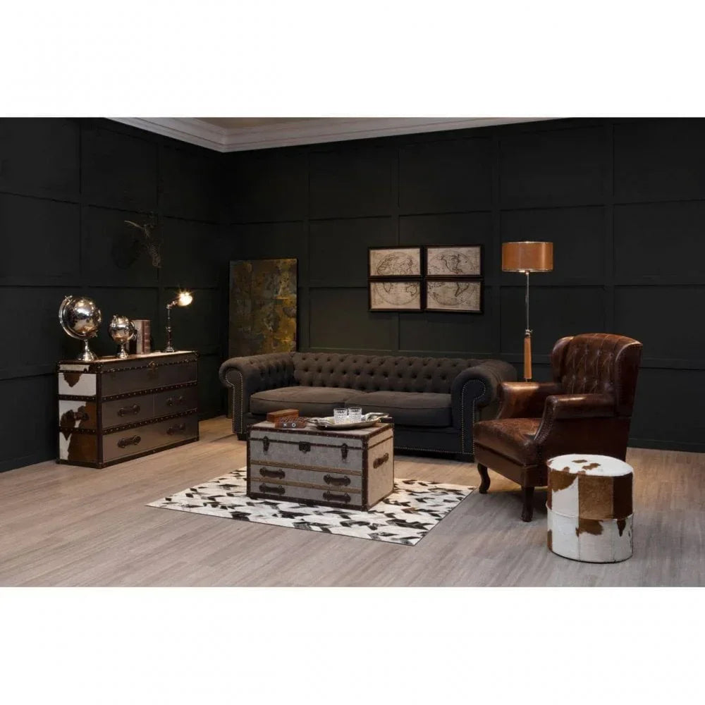 Chesterfield sofa with trunk coffee table, leather armchair and cowhide ottoman in dark lounge