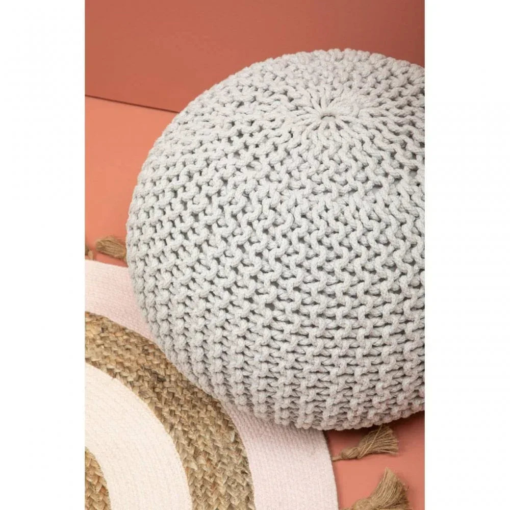 Light grey knitted pouffe on peach rug with woven jute mat and tassel detail