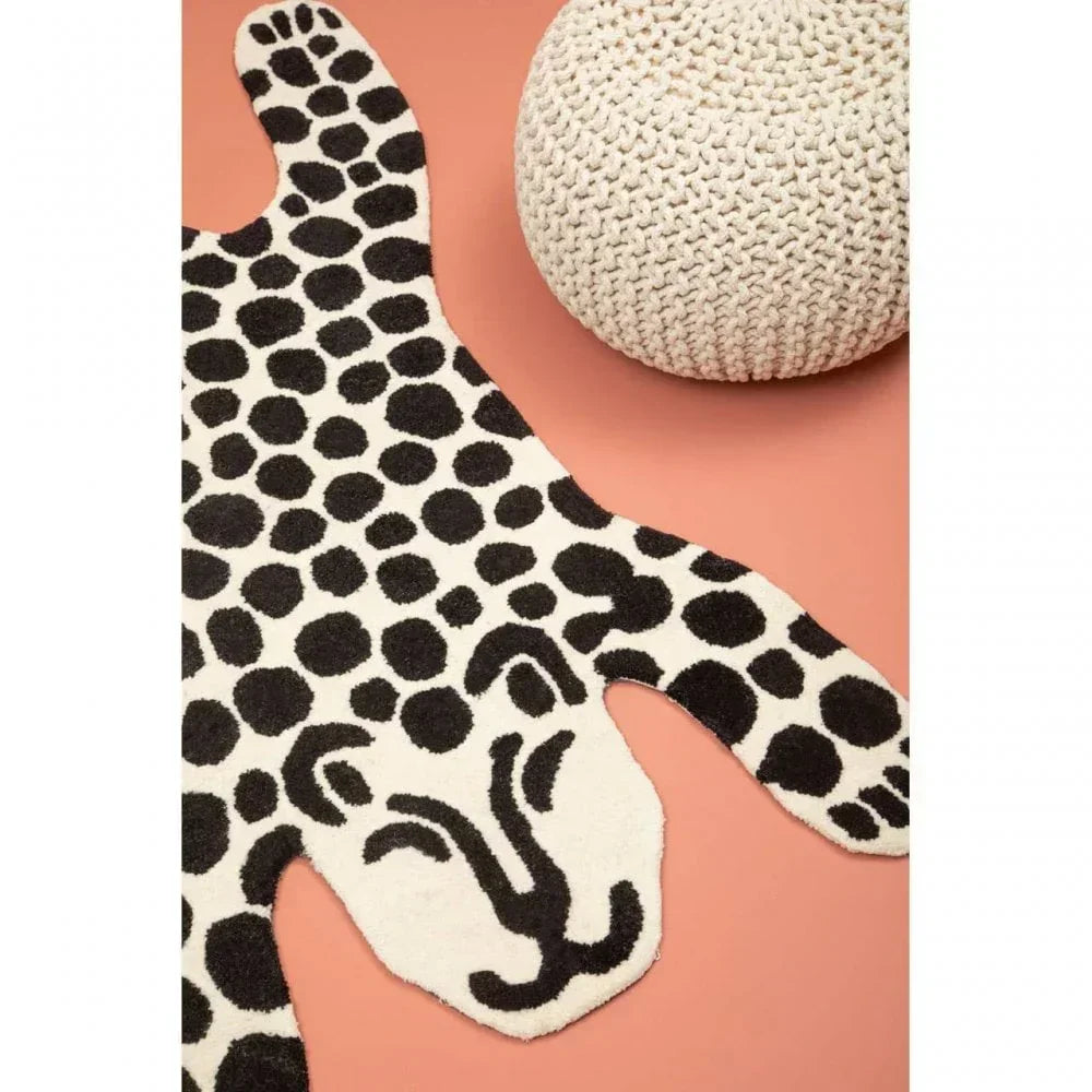 Leopard print rug with black spots beside a knitted cream pouffe on peach floor