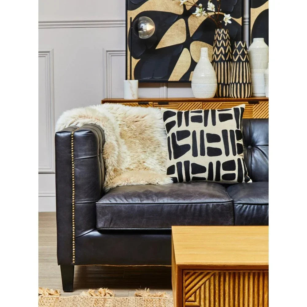 Black leather sofa with gold stud trim, geometric cushion, and faux fur throw in living room