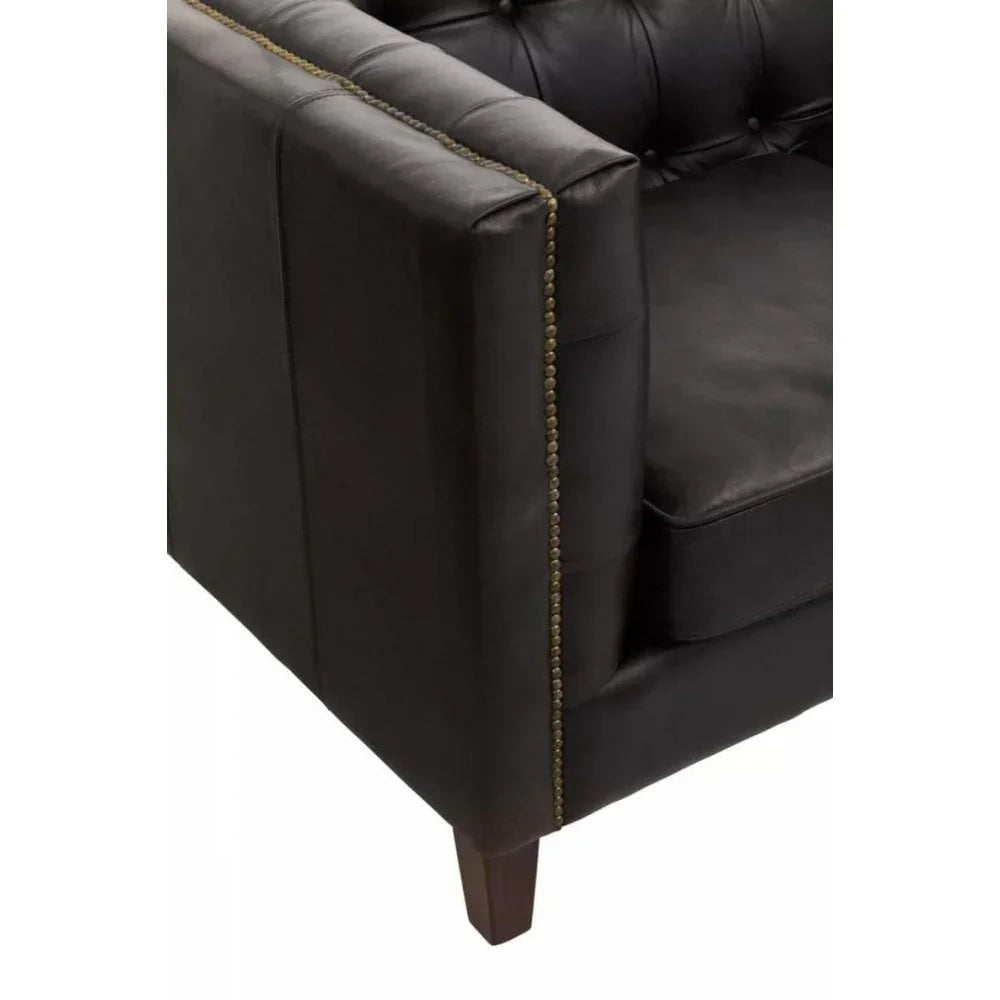 Close-up of black leather sofa arm with brass nailhead trim and dark wooden leg