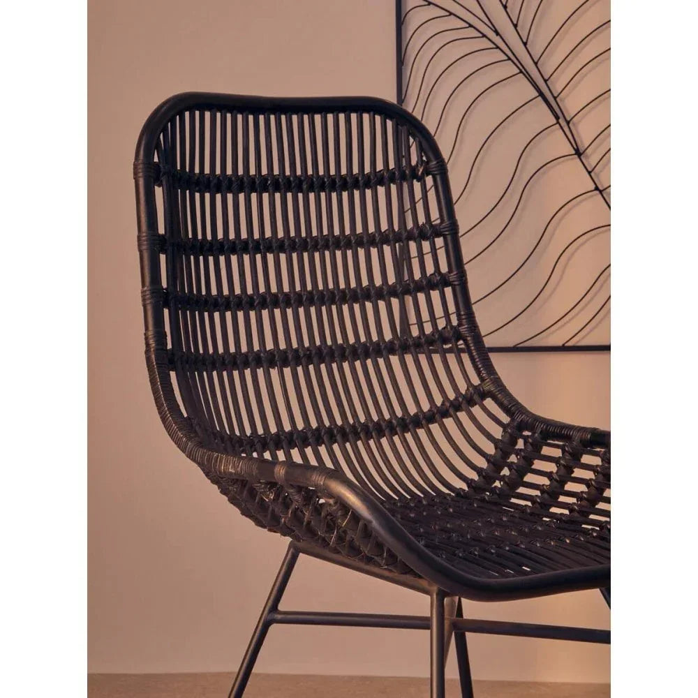 Black rattan chair with metal frame, curved backrest, close-up angle against neutral wall