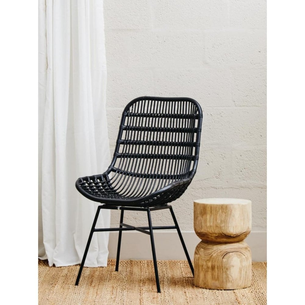 Black rattan dining chair with metal legs beside wooden accent stool on woven rug