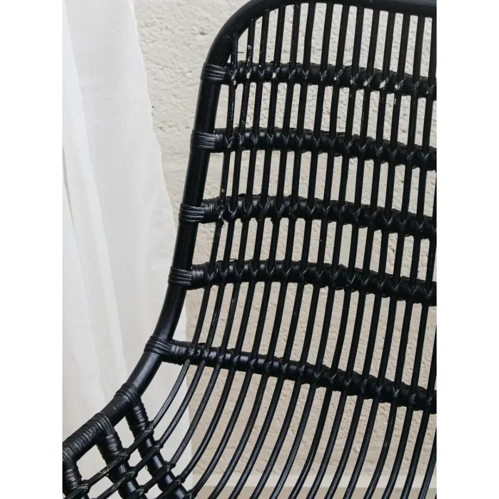Black rattan chair backrest with woven detail against cream wall and white curtain
