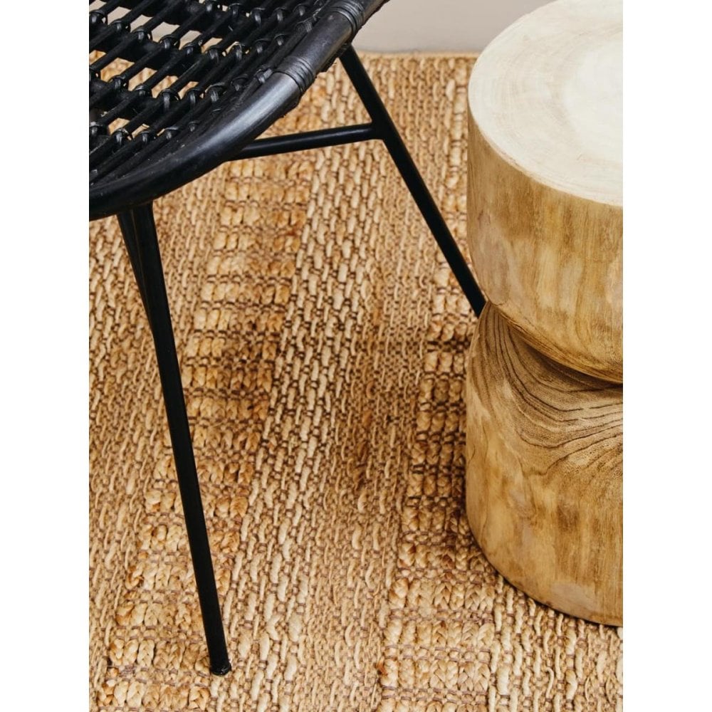 Black rattan chair with metal legs beside round wooden table on textured jute rug