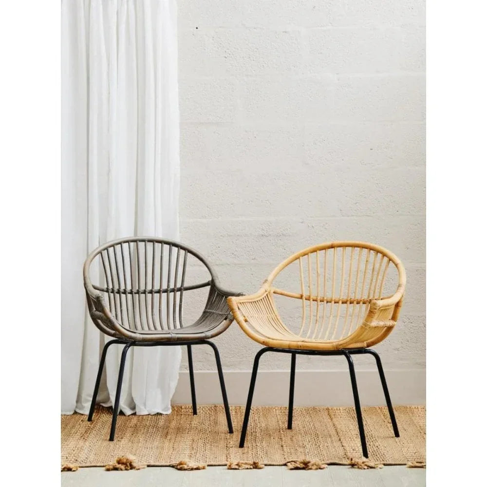 Pair of rattan chairs with black metal legs on woven rug against a light wall