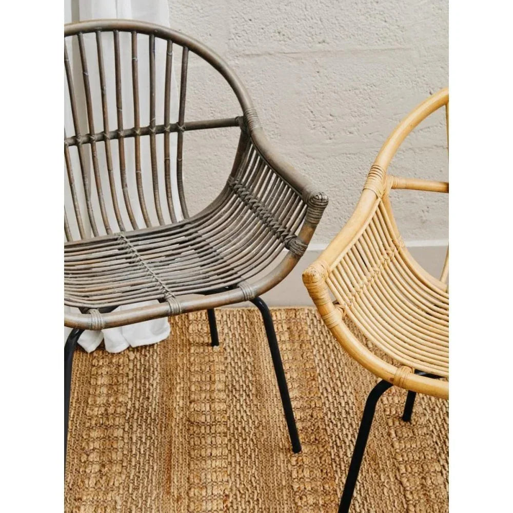 Pair of rattan dining chairs with black metal legs on woven rug against textured wall