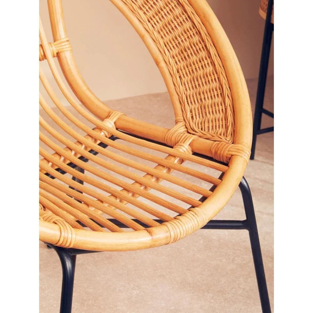 Curved rattan chair seat with woven backrest and black metal legs on beige floor