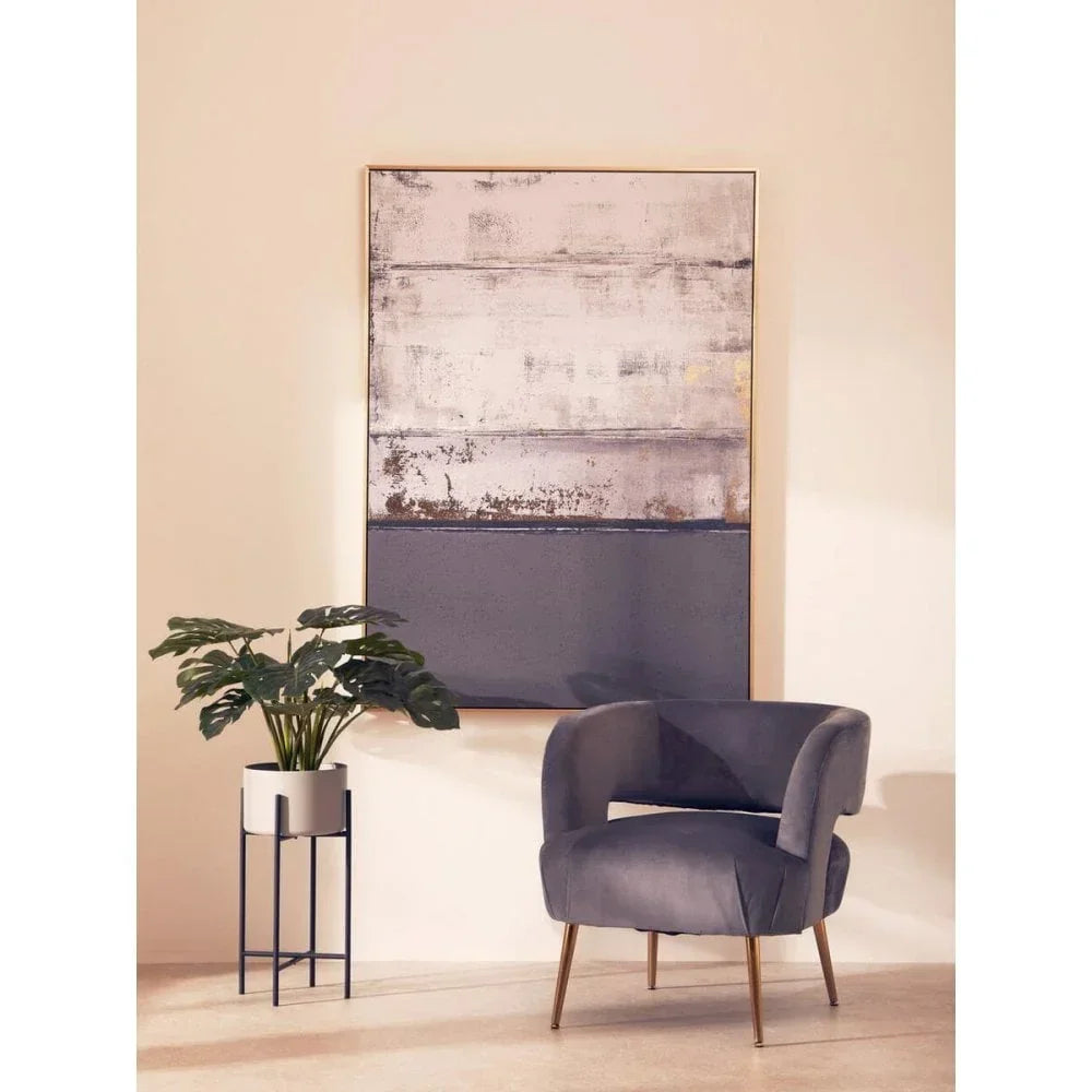 Grey velvet accent chair with gold legs beside potted plant and abstract wall art